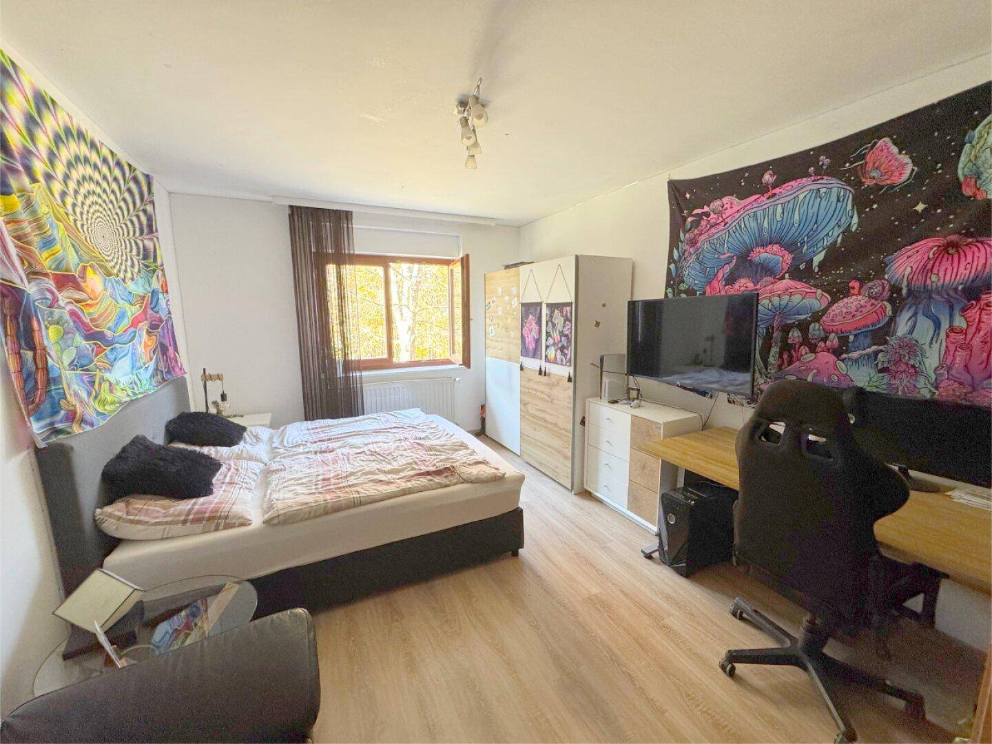 Schlafzimmer mit Laminatboden, Doppelbett und farbenfroher Wanddekoration.