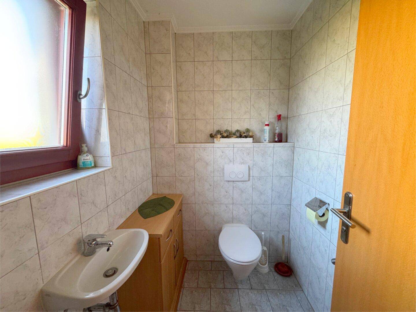 Gäste-WC mit Fenster, wandmontierter Toilette und kleinem Waschbecken.