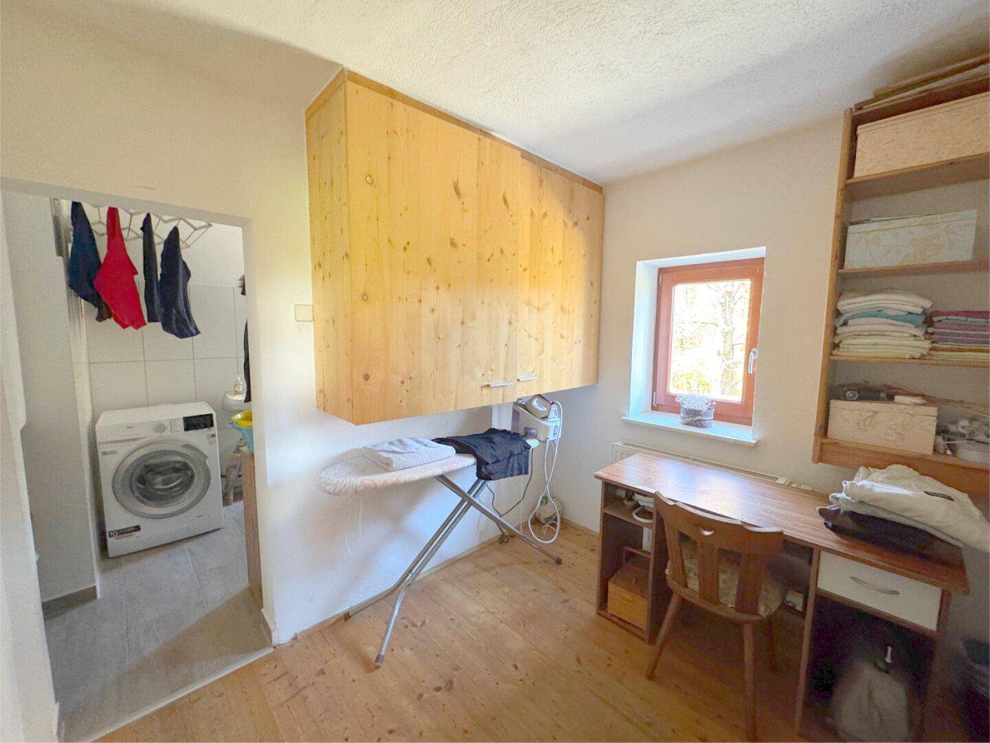 Praktischer Hauswirtschaftsraum mit Waschmaschine, Bügelbrett und Holzschränken.