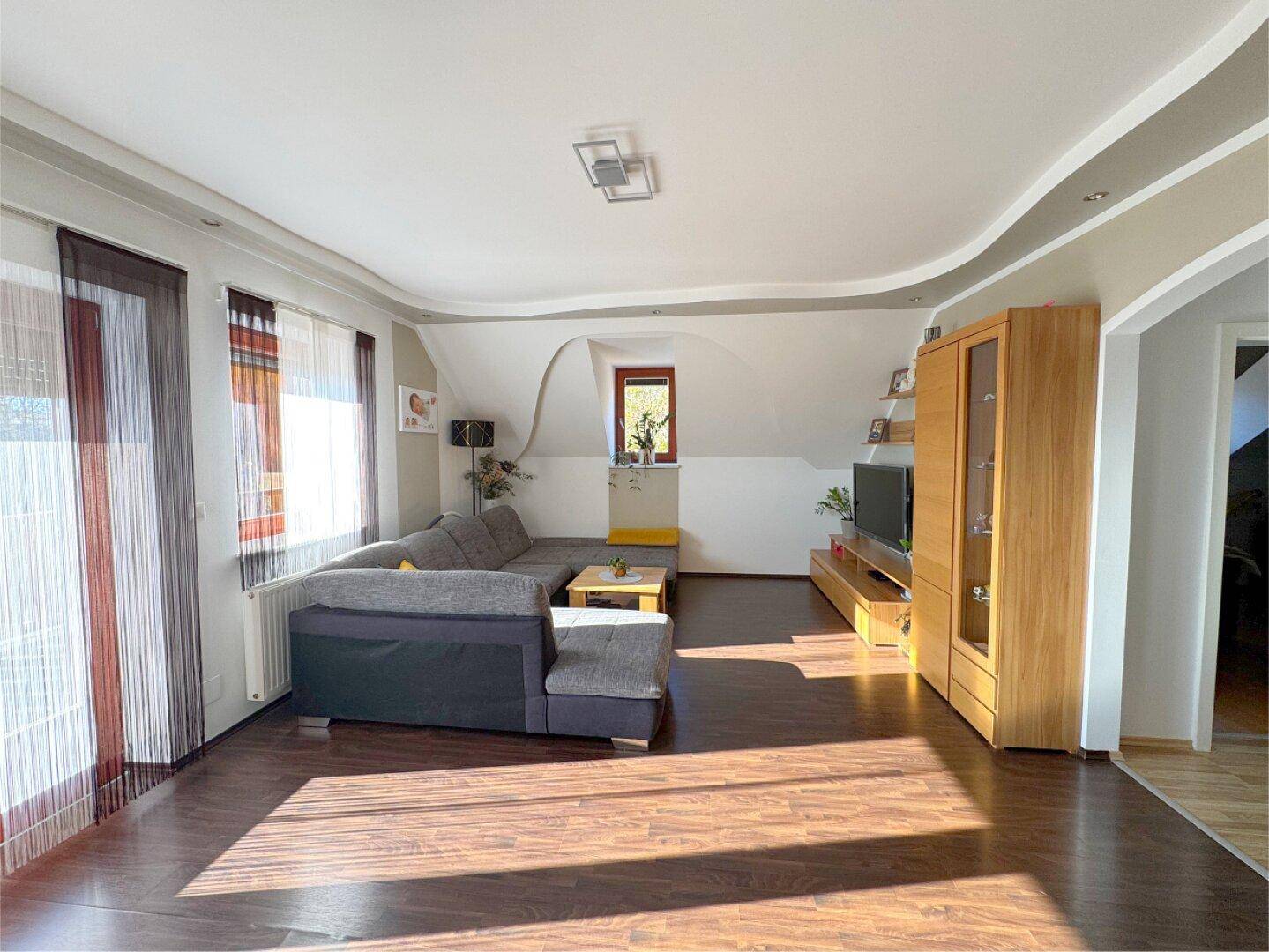 Geräumiges Wohnzimmer im Dachgeschoss mit großem Ecksofa und dunklem Laminatboden.
