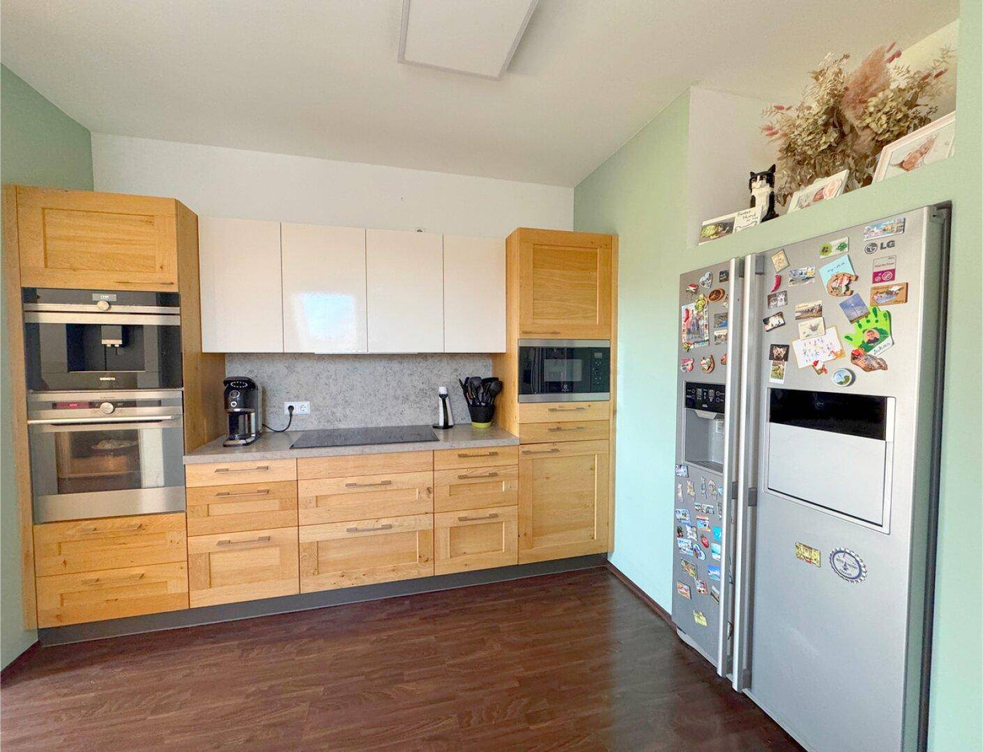 Moderne Küche im Dachgeschoss mit Holzelementen, Einbaugeräten und großem Kühlschrank.