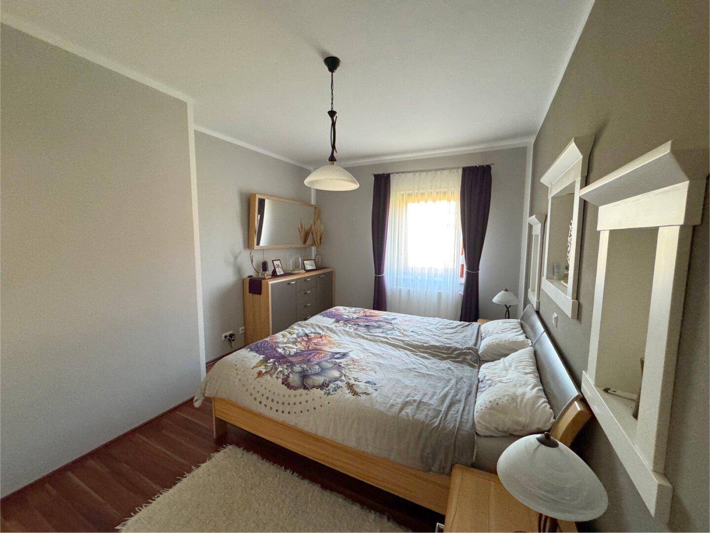 Schlafzimmer mit Doppelbett, Nachttischen und einem großen Fenster für Tageslicht.