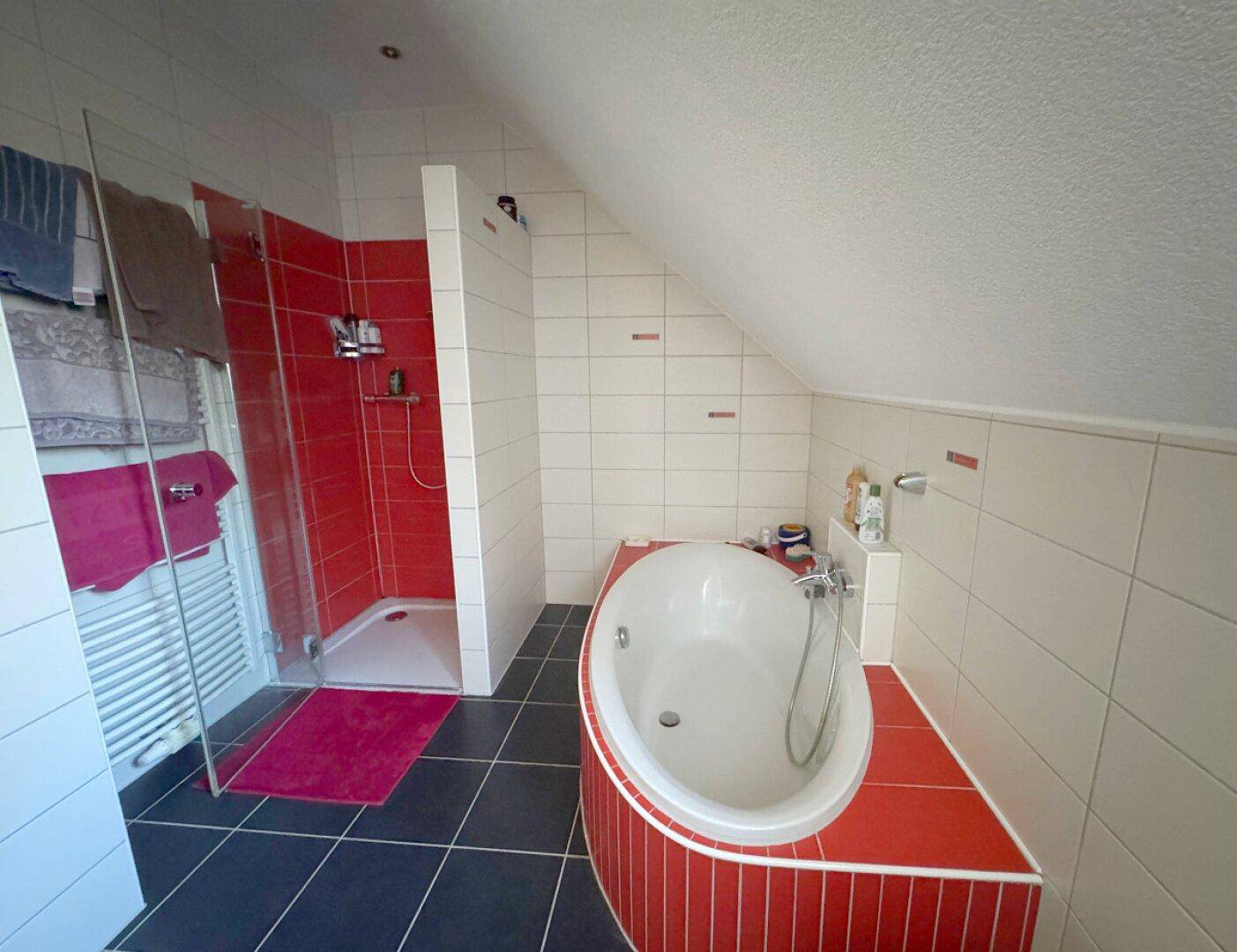 Modernes Badezimmer im Dachgeschoss mit Badewanne, Dusche und roten Akzentfliesen.