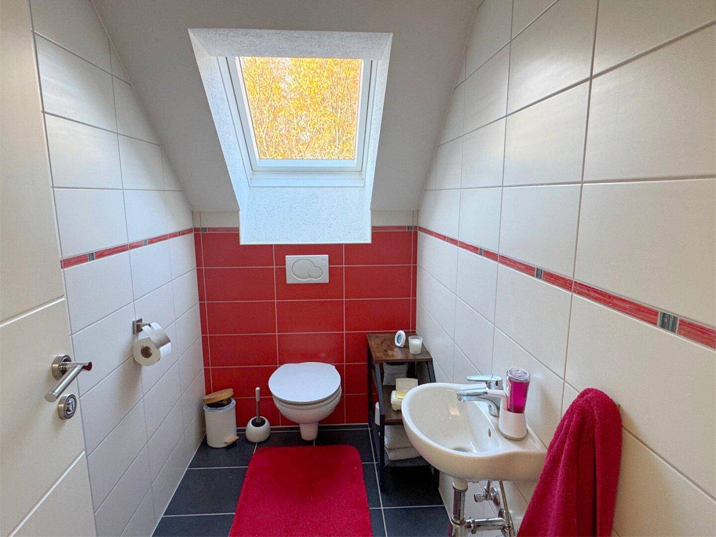 Gäste-WC im Dachgeschoss mit Dachfenster, wandmontierter Toilette und modernen Fliesen.