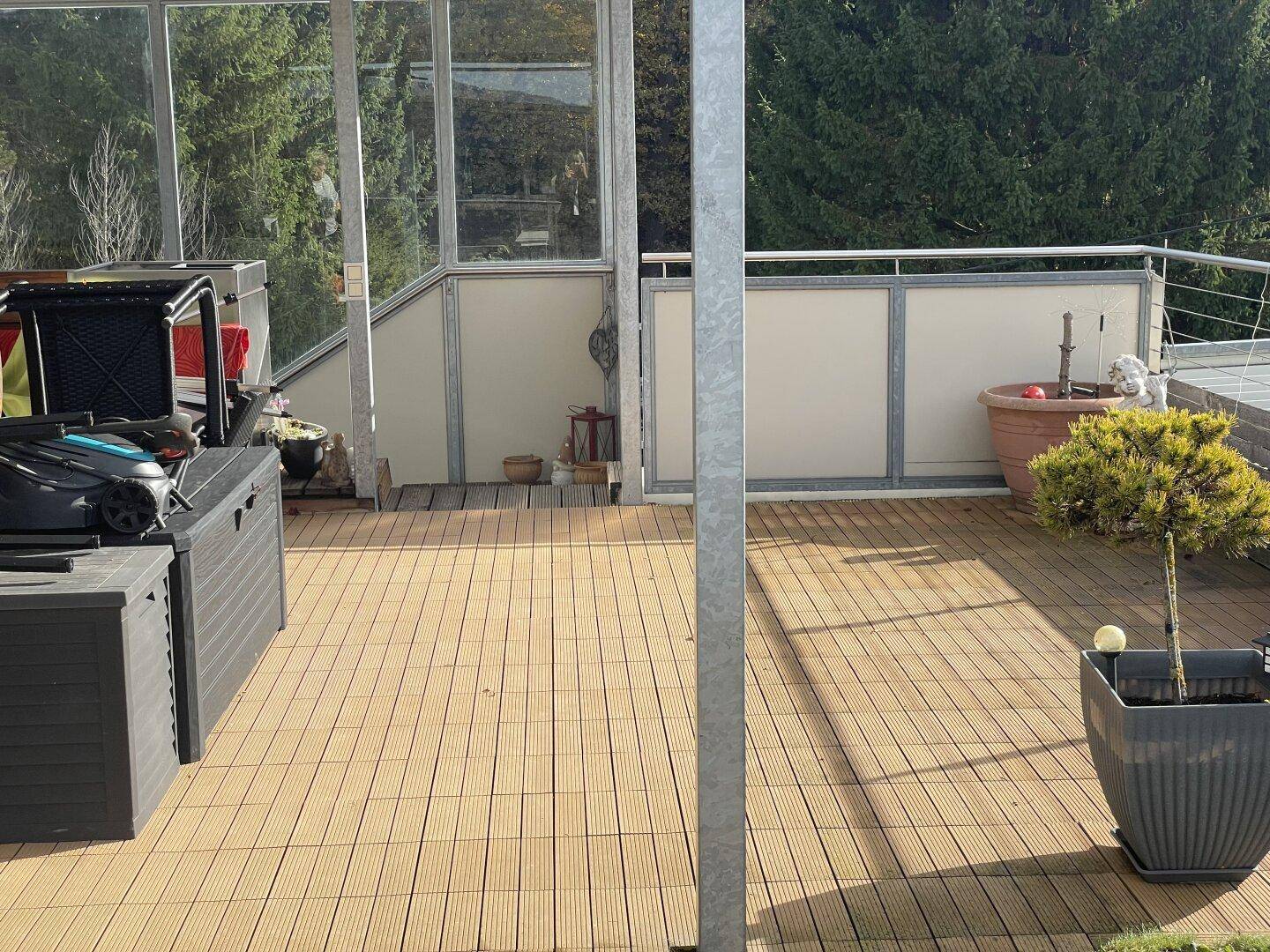 Geräumige Dachterrasse mit Holzfliesen, Stauraum und Blick ins Grüne.