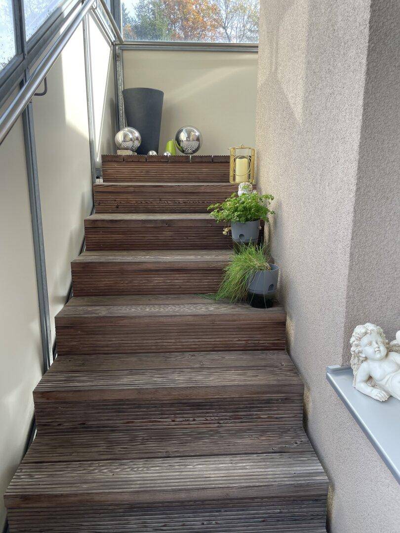 Außentreppe aus Holz mit dekorativen Elementen, die zu einer oberen Ebene führt.