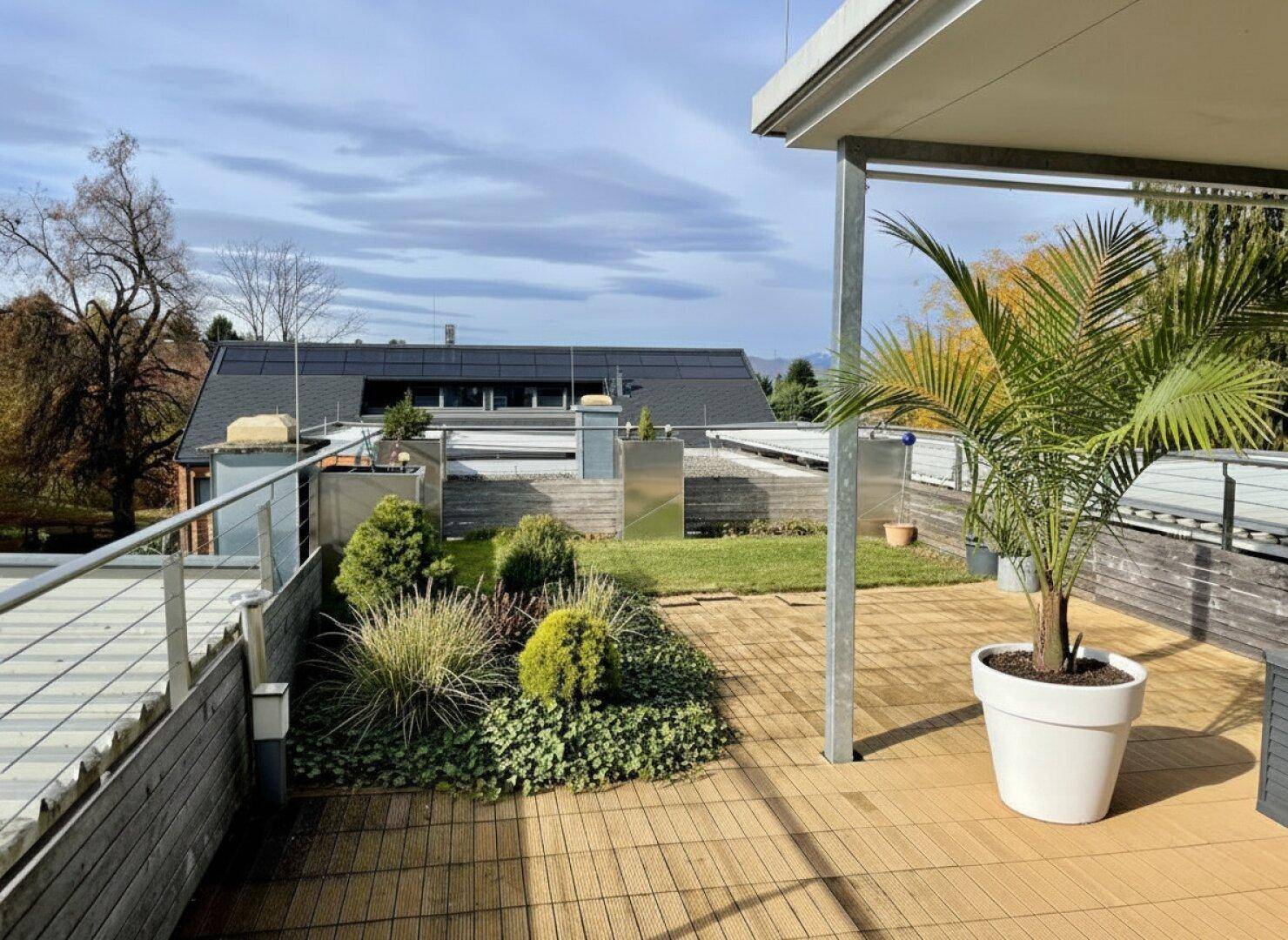 Weitläufige Dachterrasse mit Holzbelag, Grünflächen und Blick auf die Dächer.