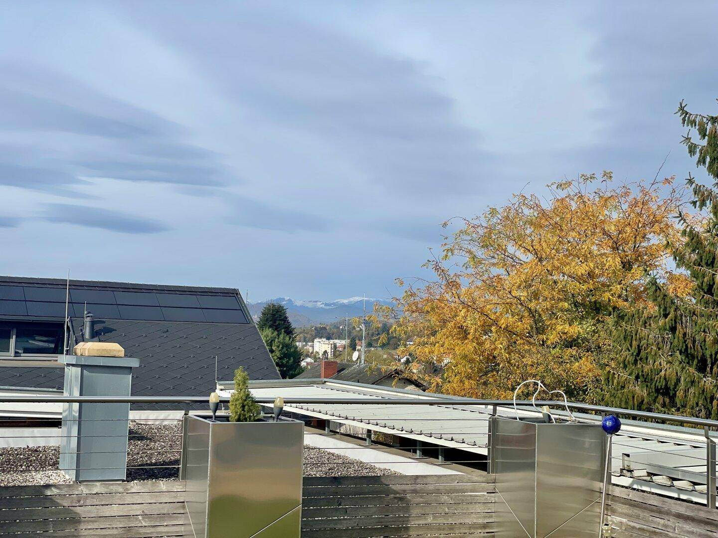 Weitblick von der Dachterrasse über die Dächer mit herbstlicher Vegetation und Bergen im Hintergrund.