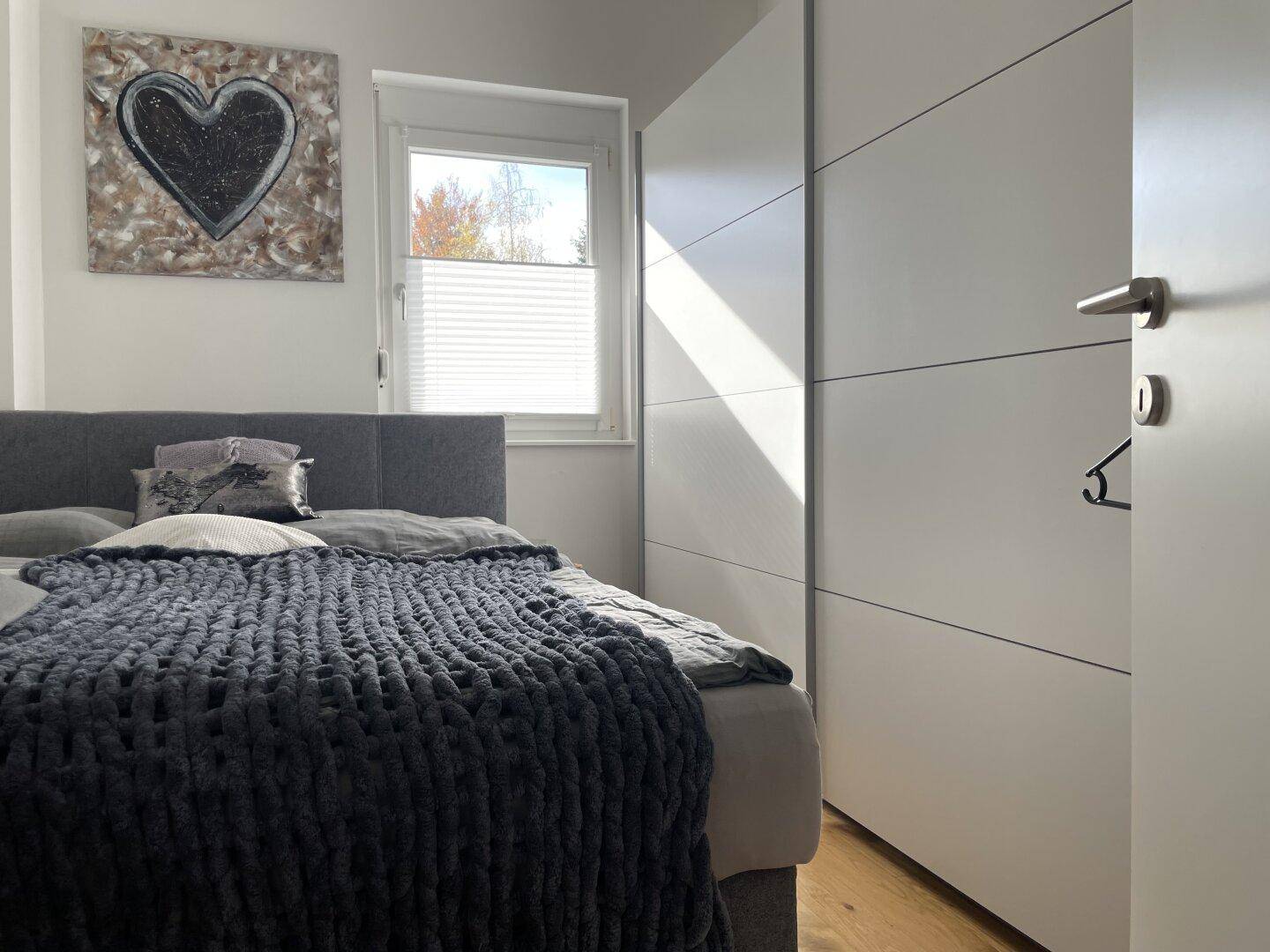 Modernes Schlafzimmer mit Holzboden, großem Kleiderschrank und Fenster.