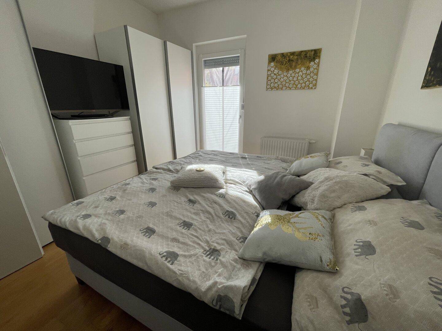 Gemütliches Schlafzimmer mit Doppelbett, Holzboden und Fenster mit Jalousien.