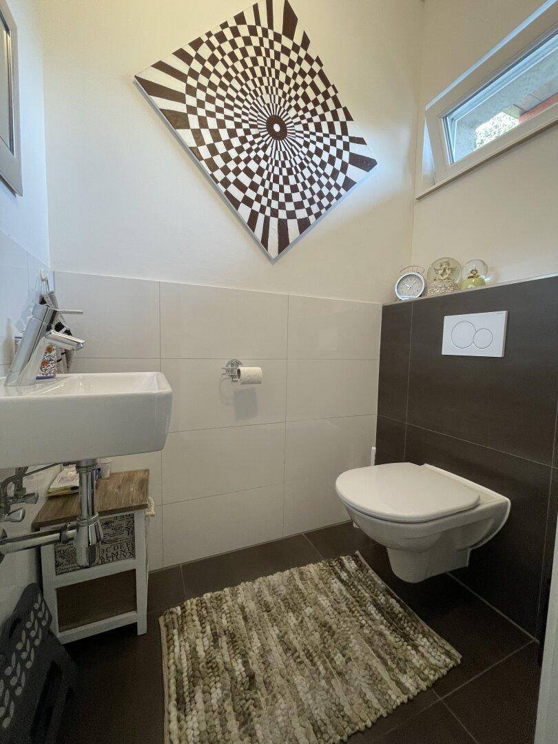 Modernes Gäste-WC mit wandhängendem WC, kleinem Waschbecken und Fenster.