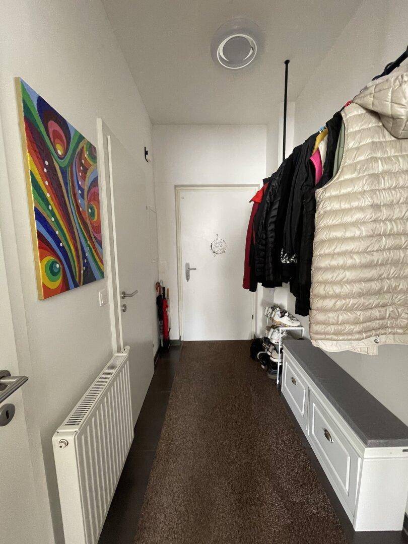 Heller Eingangsbereich mit Garderobe, Schuhbank und farbenfrohem Kunstwerk.