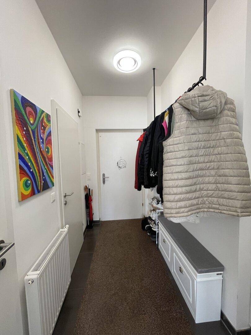 Eingangsbereich mit Garderobe, Schuhbank und farbenfrohem Kunstwerk an der Wand.