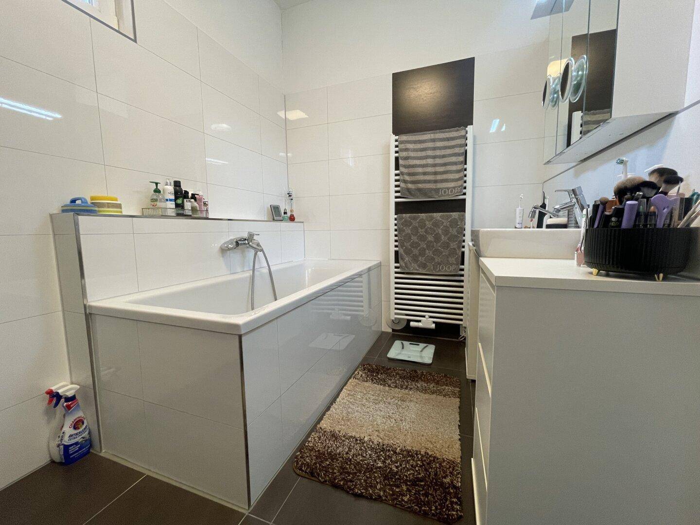 Modernes Badezimmer mit Badewanne, weißen Fliesen und beheiztem Handtuchhalter.