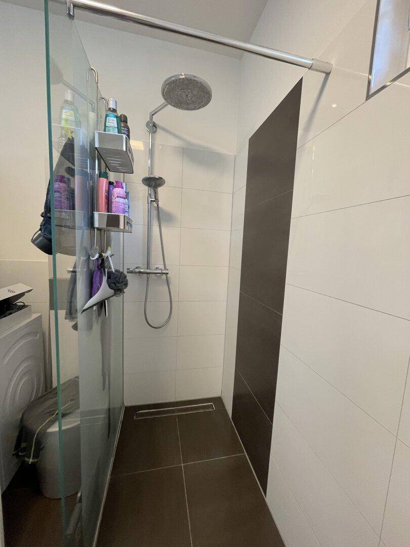 Modernes Badezimmer mit ebenerdiger Dusche, dunklen Bodenfliesen und Waschmaschine.