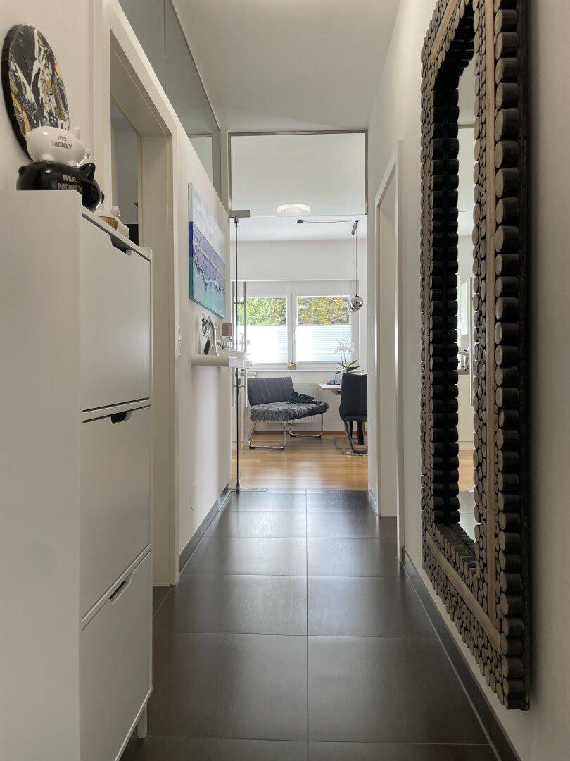 Heller Flur mit dunklen Fliesen, einem großen Spiegel und Blick in den Wohnbereich.