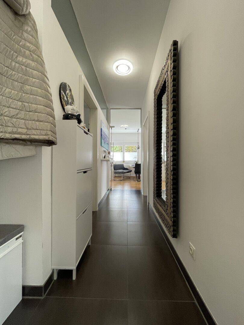 Moderner Flur mit dunklen Fliesen, einem großen Spiegel und indirekter Beleuchtung.