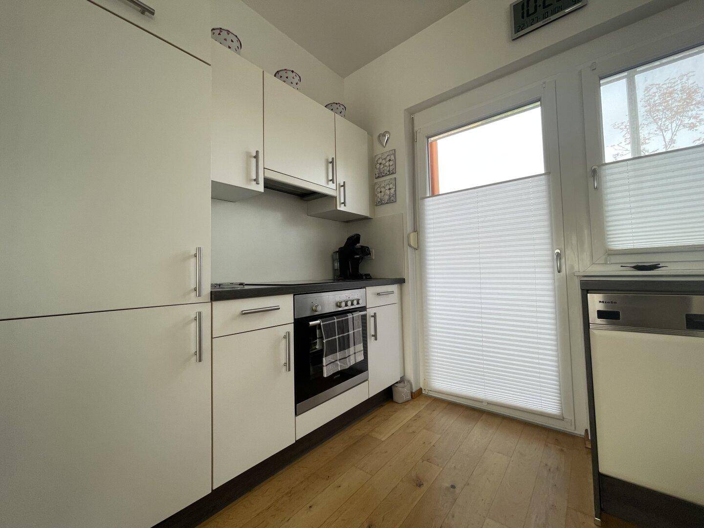 Moderne Küche mit weißen Schränken, integriertem Backofen und Holzboden.