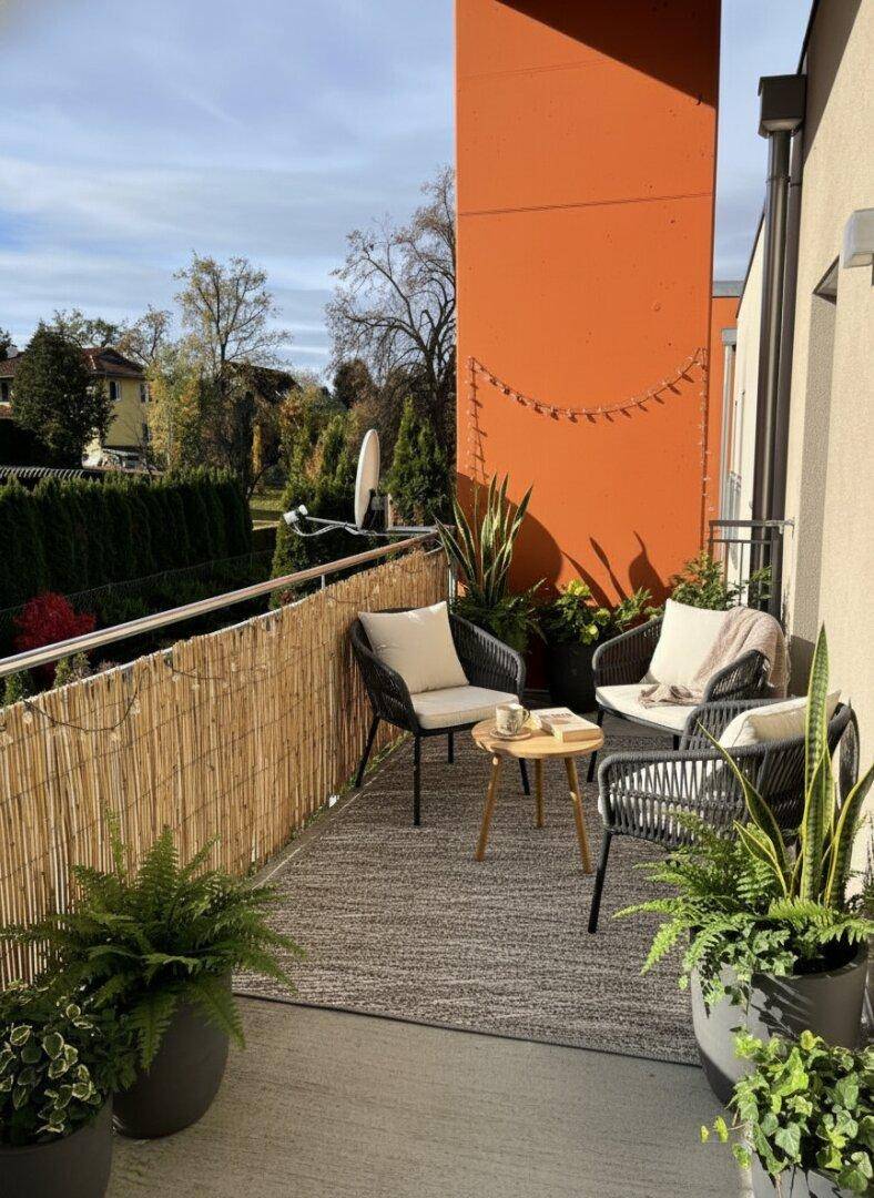 Gemütlicher Balkon mit Sitzgelegenheiten, Pflanzen und Bambus-Sichtschutz.