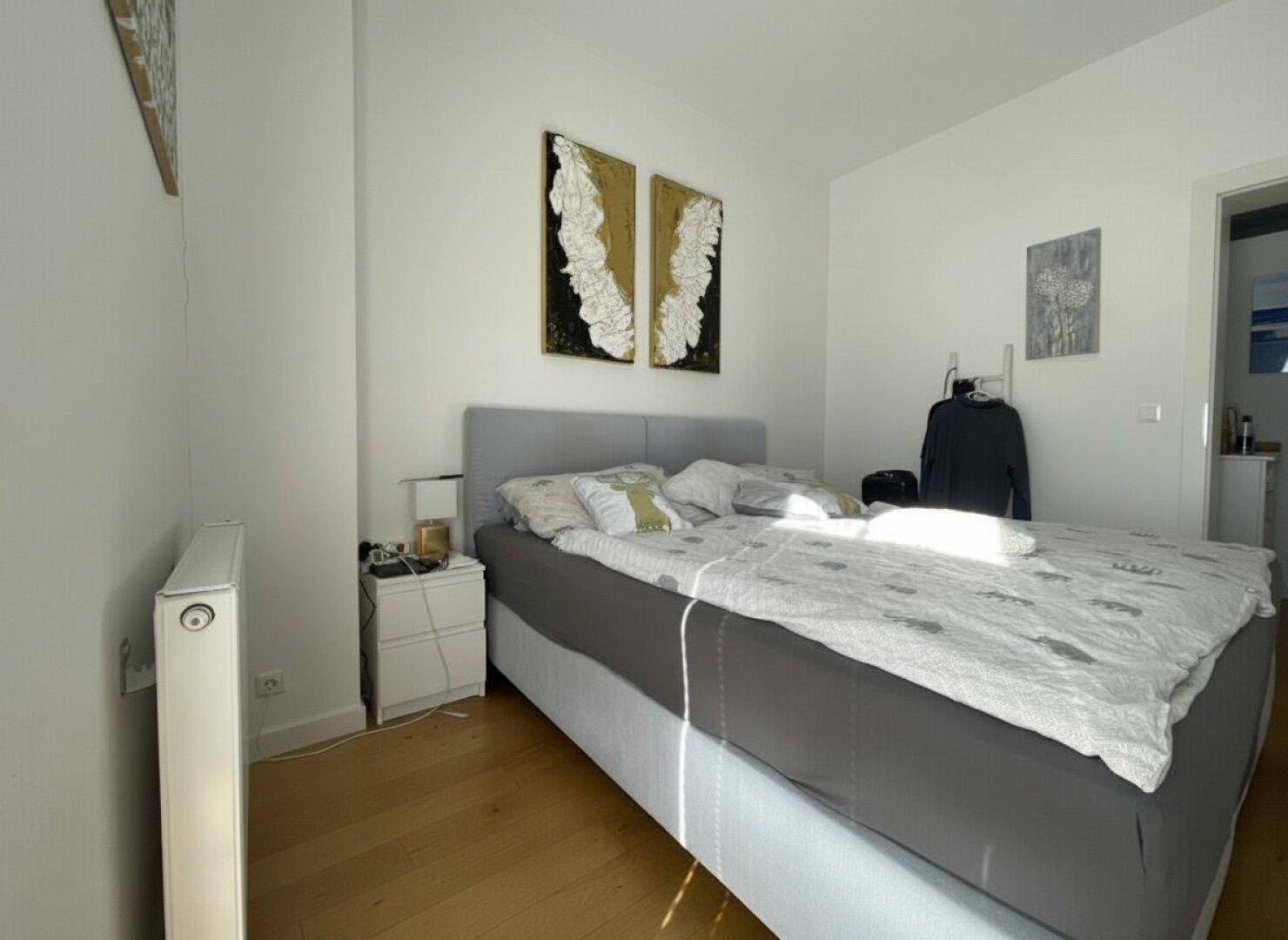 Helles Schlafzimmer mit Holzboden, Doppelbett und moderner Wanddekoration.