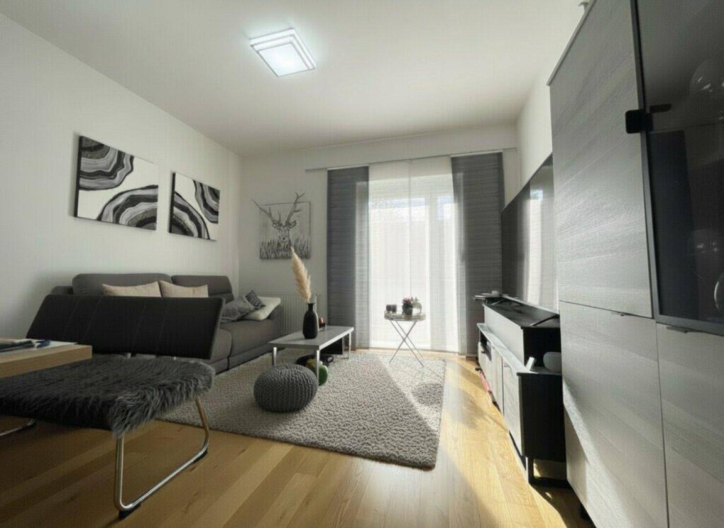 Helles Wohnzimmer mit Holzboden, Sofa, Teppich und Zugang zum Balkon.