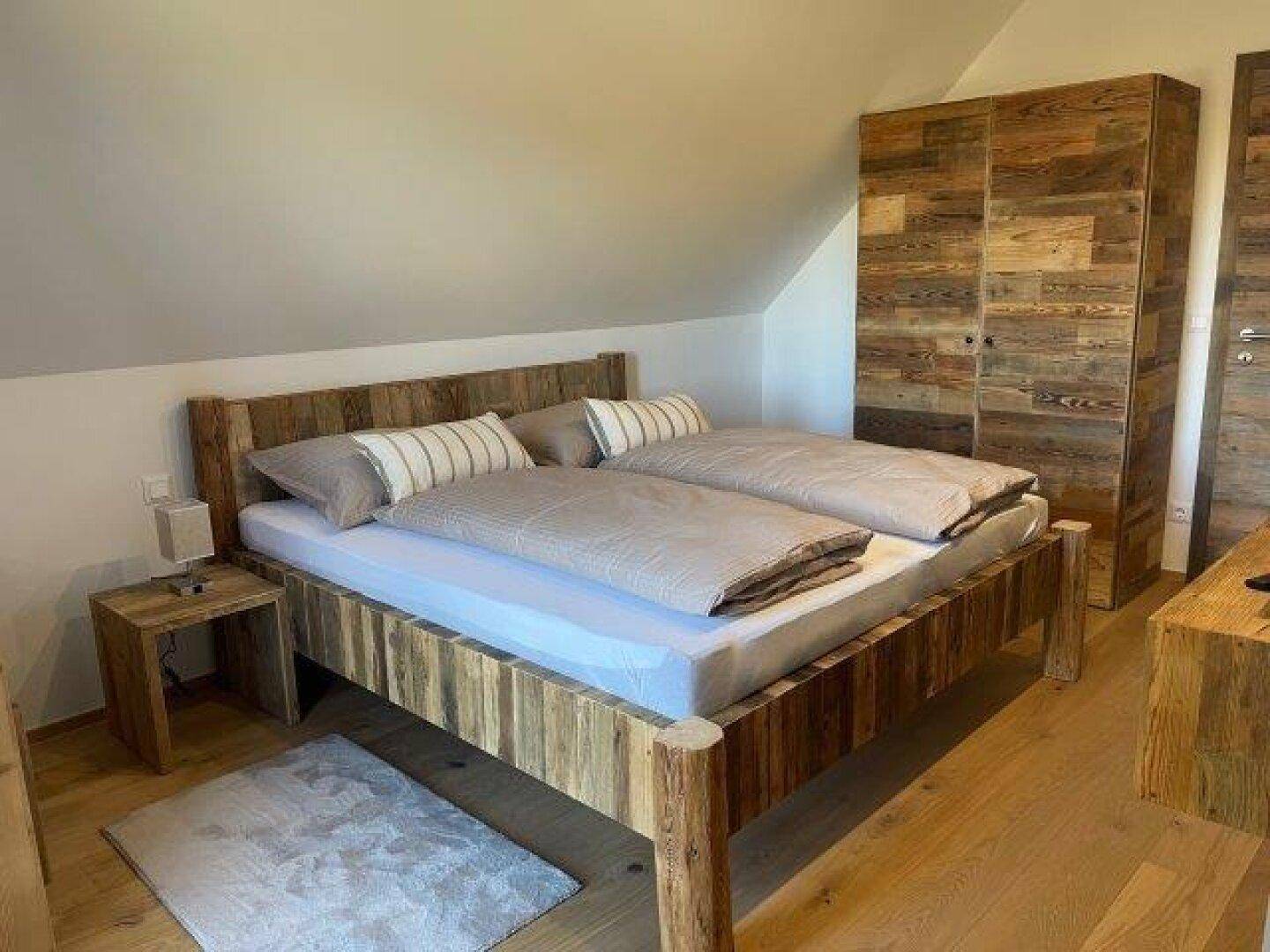Gemütliches Schlafzimmer mit rustikalem Holzbett, Holzschrank und Holzboden unter einer Dachschräge.