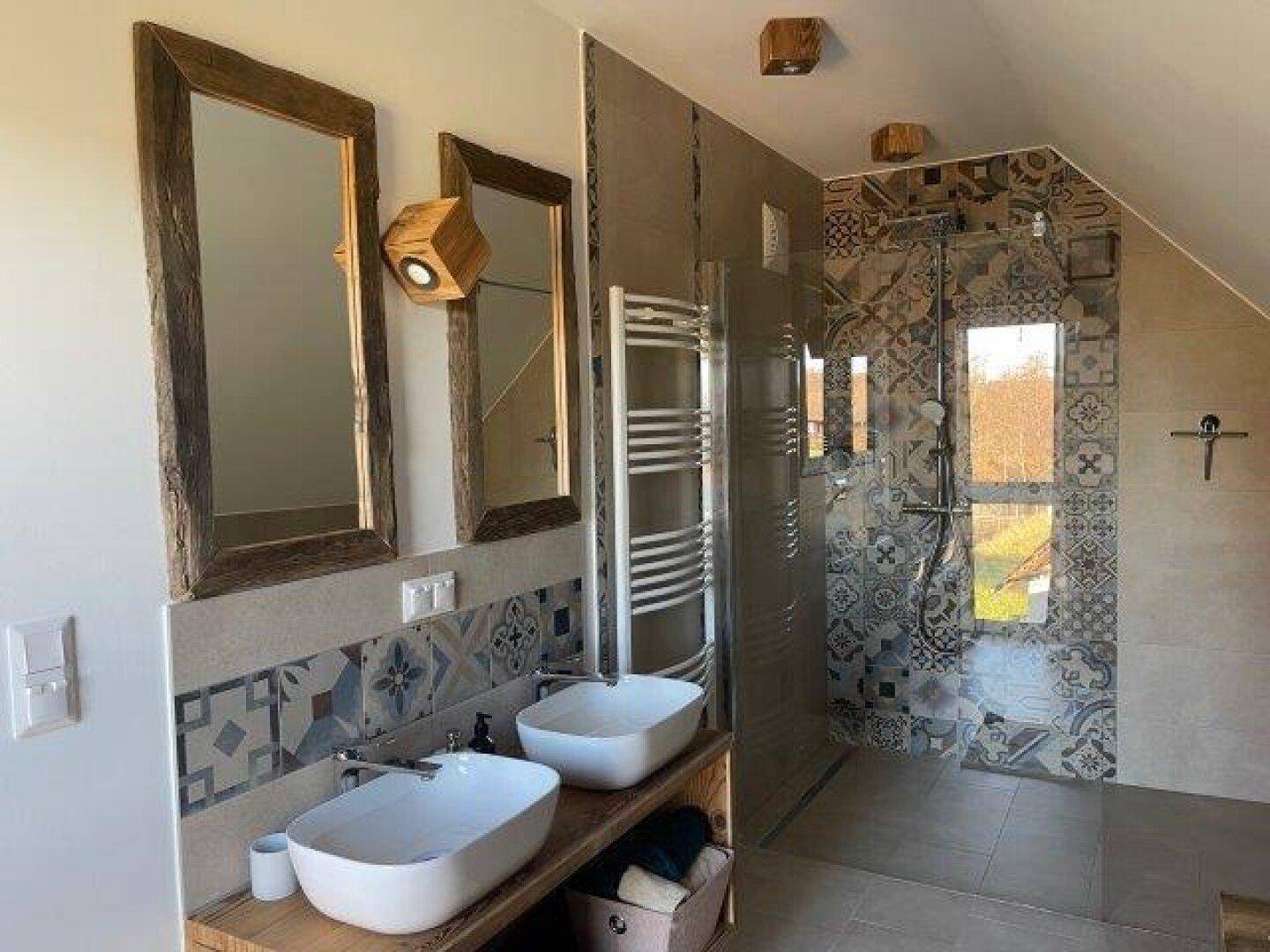 Modernes Badezimmer mit begehbarer Dusche, Doppelwaschbecken auf Holzunterschrank und dekorativen Fliesen.