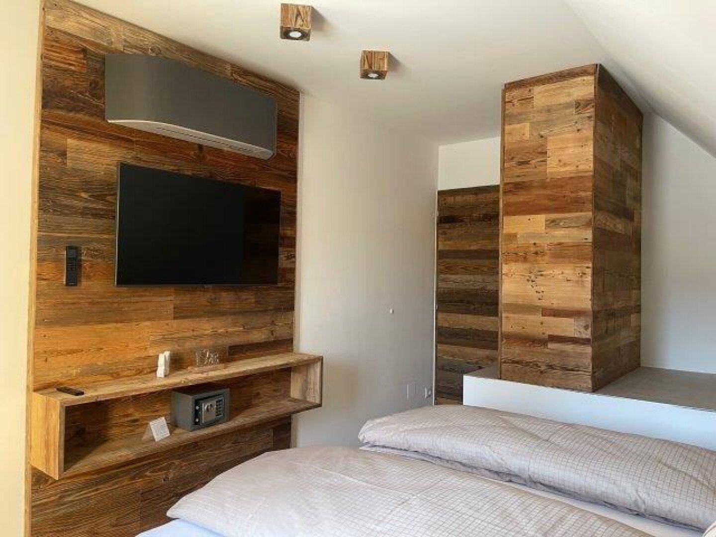 Schlafzimmer mit zwei Einzelbetten, einer Holzwand mit Fernseher und praktischem Regal unter der Dachschräge.