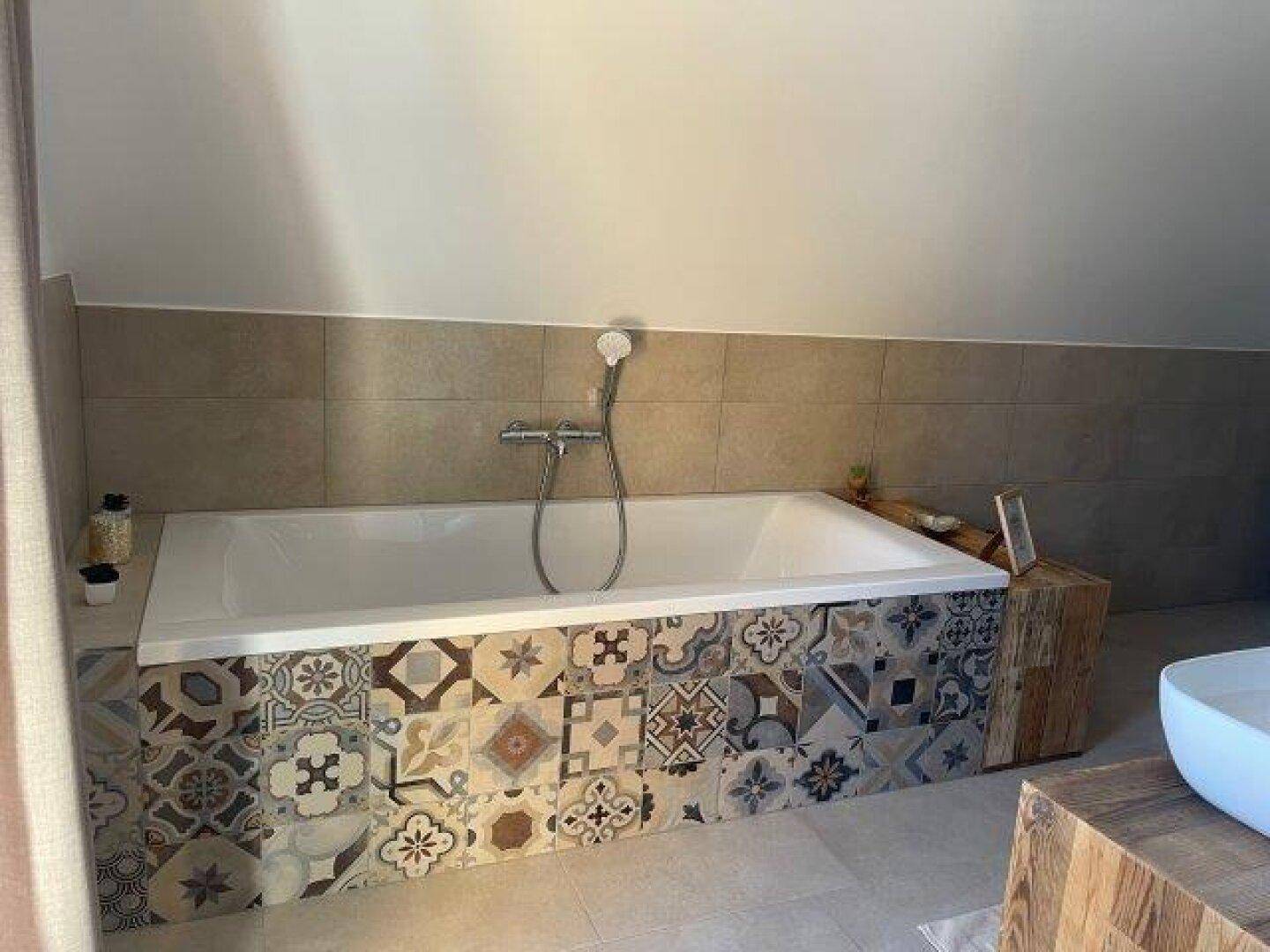 Badezimmer mit eingebauter Badewanne, dekorativen Fliesen und einer Dachschräge, die Gemütlichkeit verleiht.
