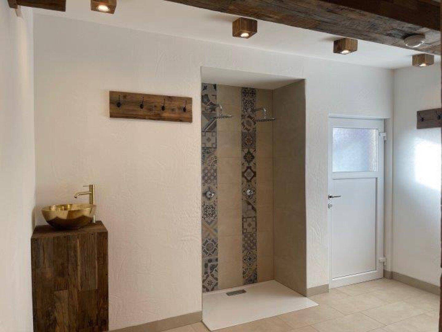 Geräumiger Duschbereich mit begehbarer Dusche und einem goldenen Waschbecken auf einem Holzunterschrank.