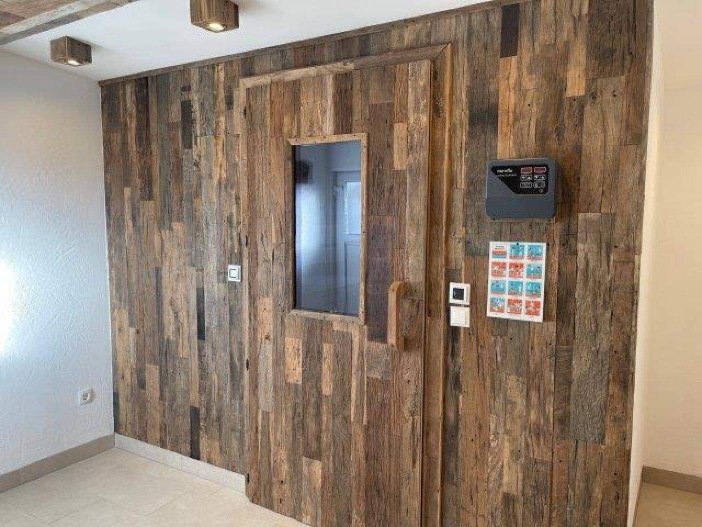 Eingangsbereich zur Sauna mit Holztür und rustikaler Holzverkleidung, inklusive Bedienfeld für die Sauna.