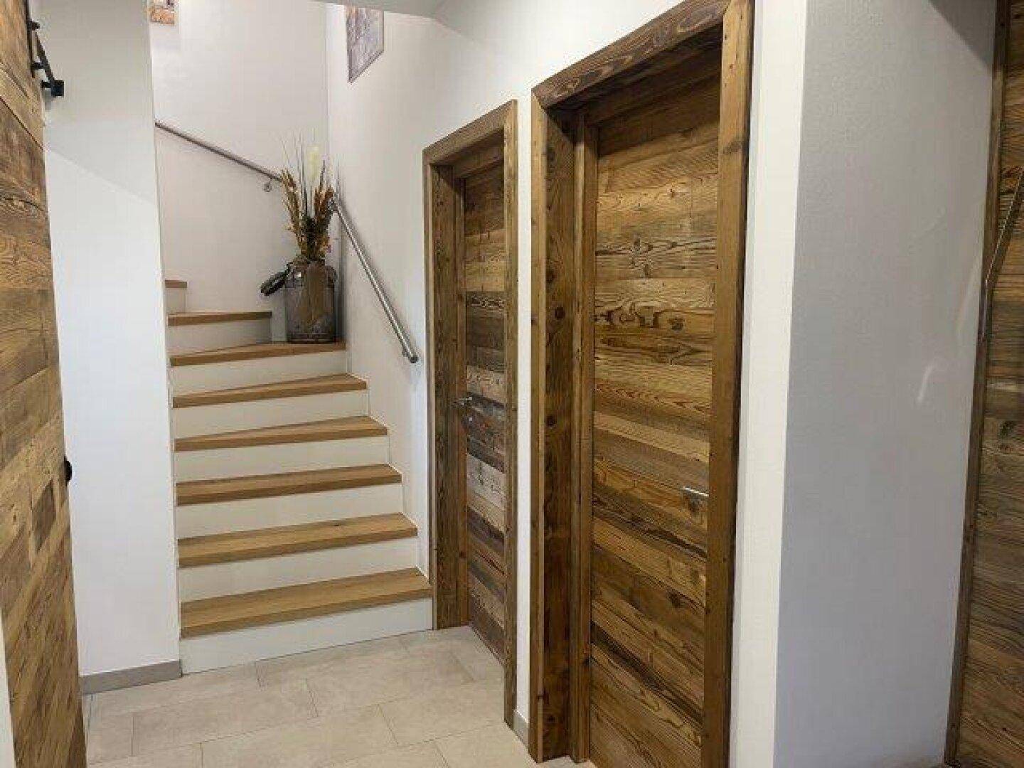 Heller Flur mit Holztreppe, Holztüren und Wandverkleidung, die zu den oberen Etagen führt.