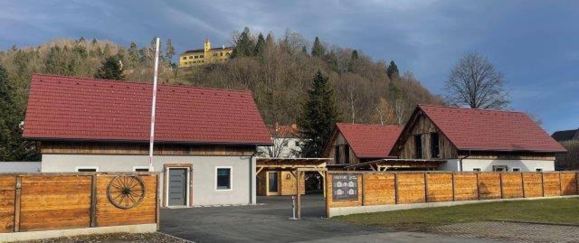 Ansicht mehrerer Häuser mit Holzzäunen und einem Hügel im Hintergrund, auf dem ein Gebäude thront.