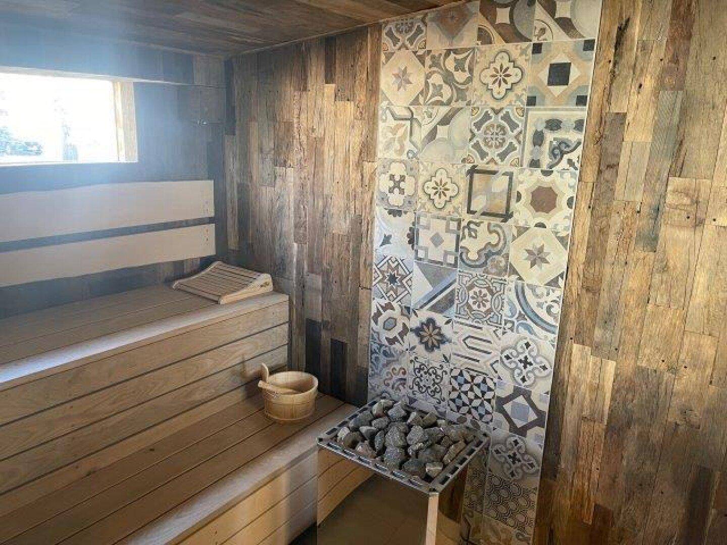 Gemütliche Sauna mit Holzbänken, Saunaofen und dekorativen Fliesen an der Wand, ideal zur Entspannung.