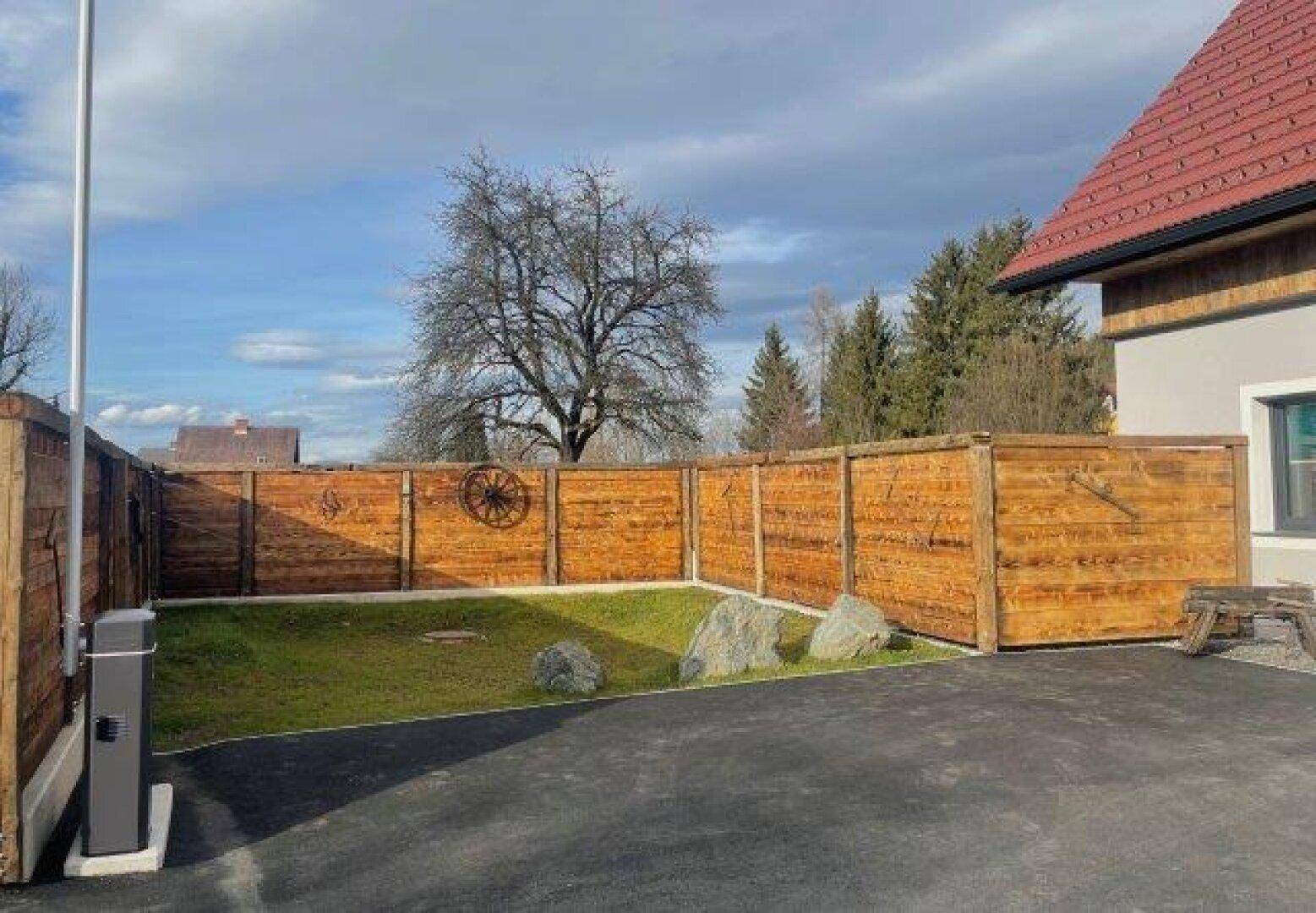 Kleiner, gepflegter Gartenbereich mit Rasen und Felsen, umgeben von einem rustikalen Holzzaun.