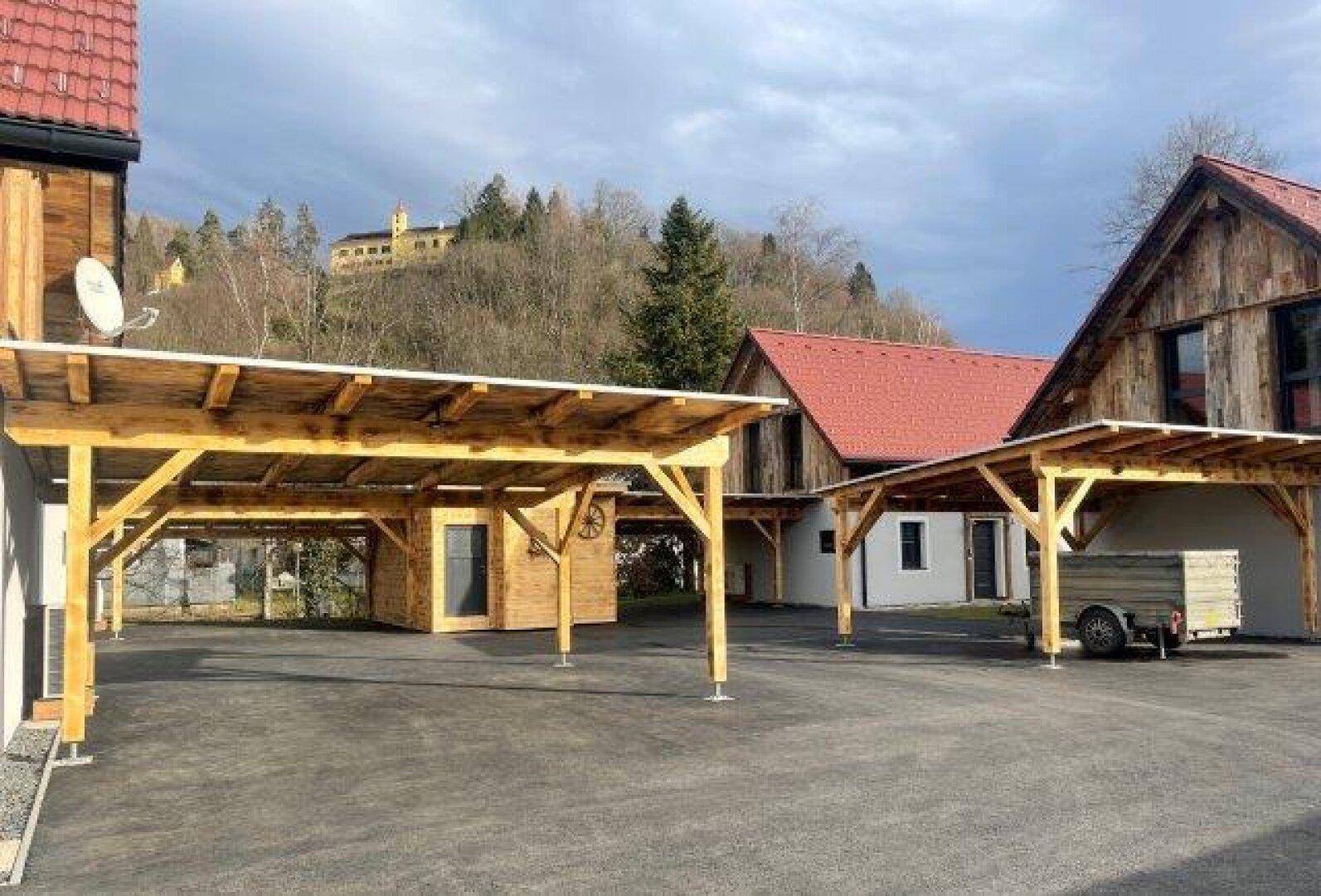 Carports vor den Häusern mit einem Hügel und einem Gebäude im Hintergrund, unter blauem Himmel.