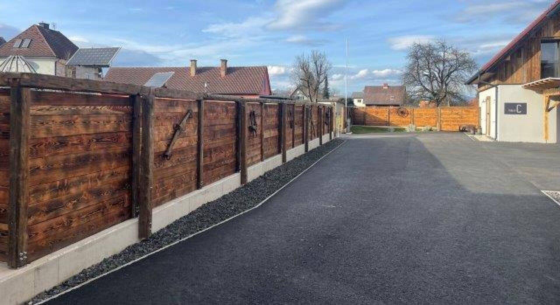 Lange gepflasterte Zufahrt entlang eines rustikalen Holzzauns, der das Grundstück begrenzt.