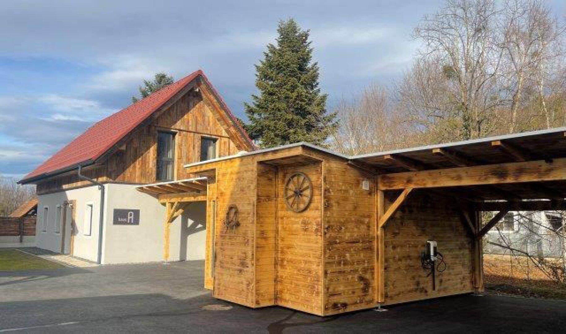 Modernes Haus mit Carport und einem Holzschuppen, ausgestattet mit einer Ladestation für Elektrofahrzeuge.