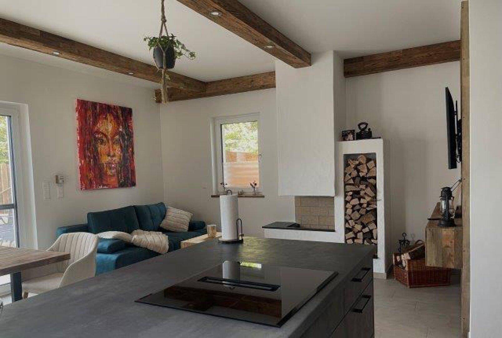 Offener Wohn- und Essbereich mit moderner Kücheninsel, Kamin und gemütlichem Sofa unter Holzbalken.