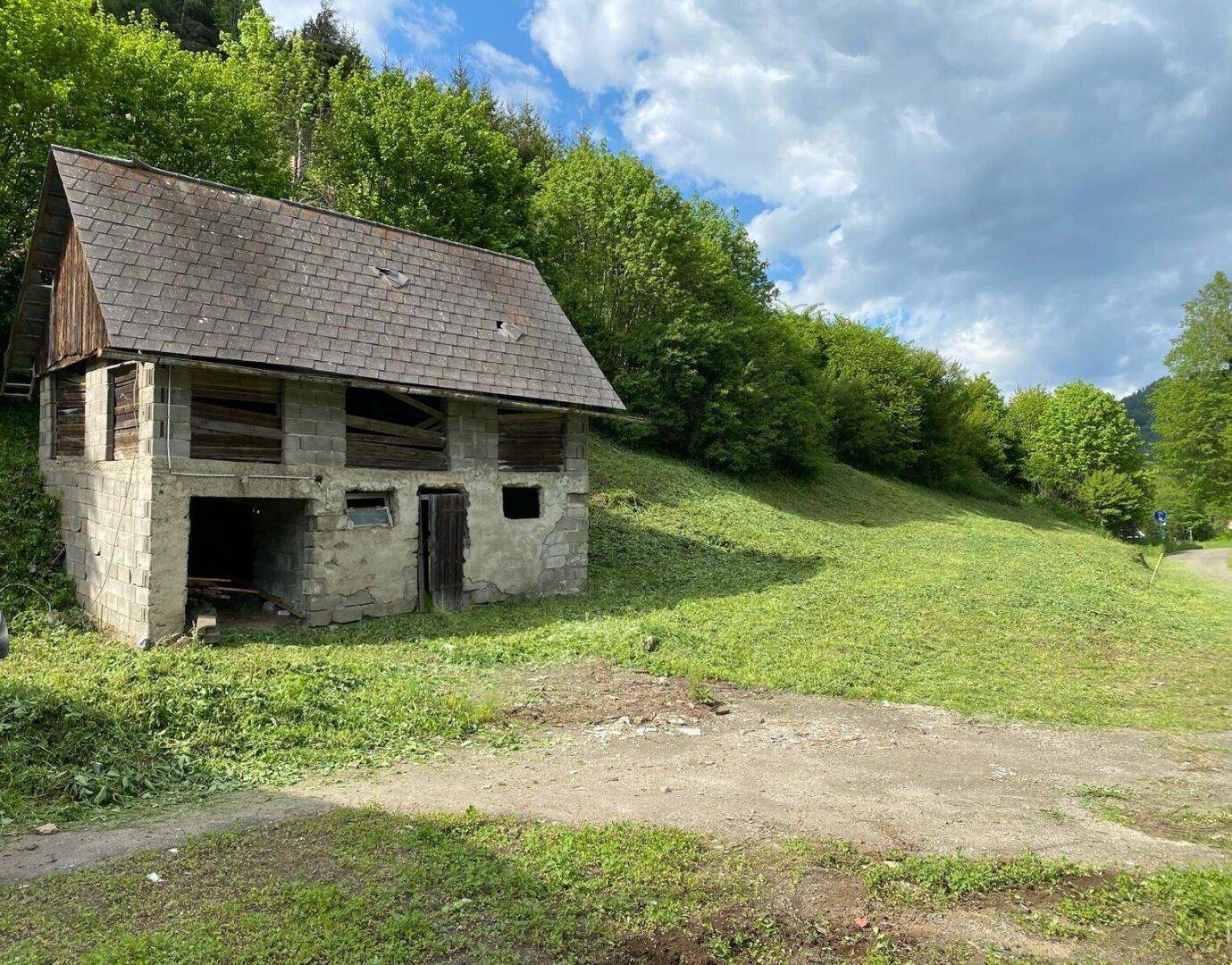 Altes, baufälliges Nebengebäude mit Steinfundament und Holzdach in ländlicher Umgebung.