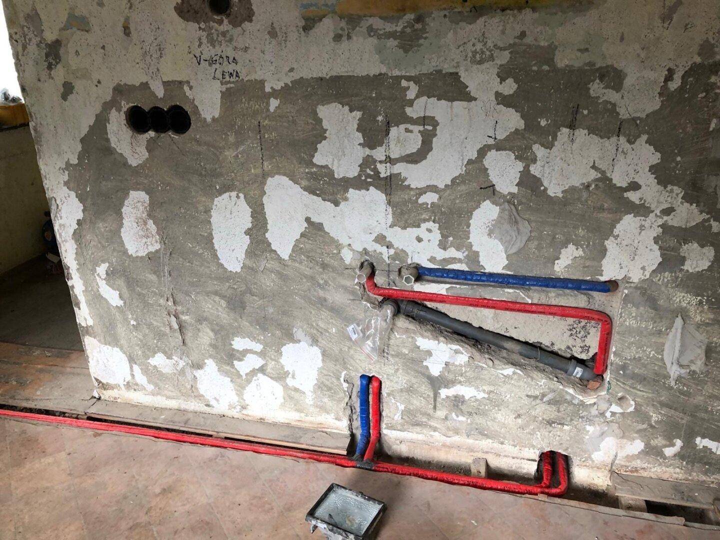 Wand mit freigelegten Wasserleitungen und Spuren von Putz, bereit für den weiteren Ausbau.
