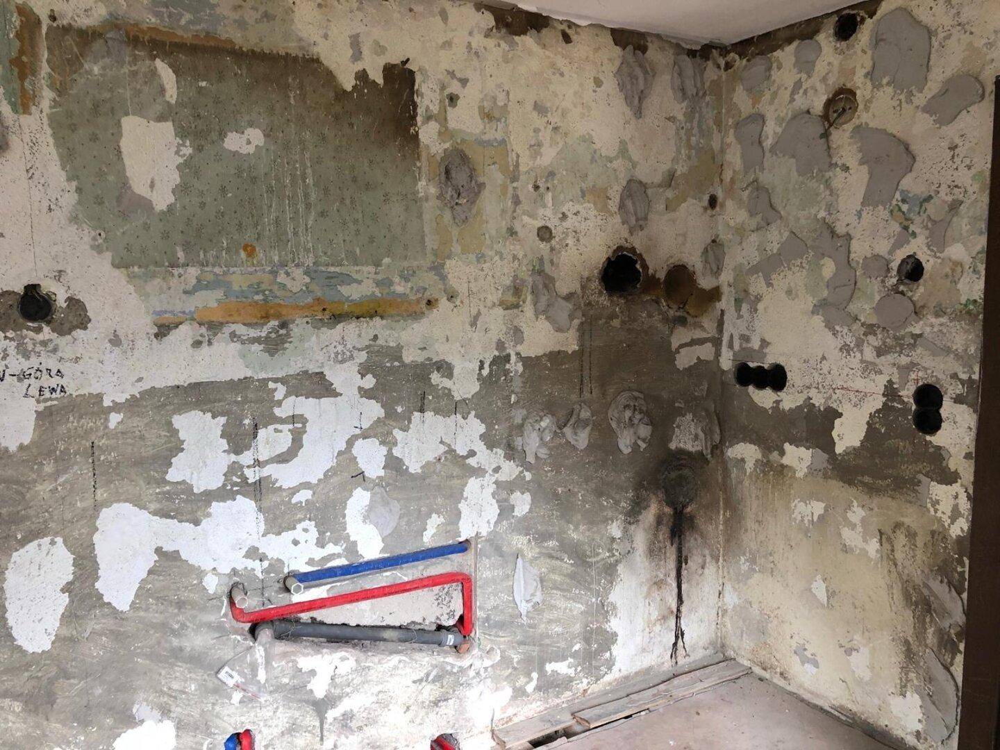 Wand mit freigelegten Leitungen und Spuren alter Tapete, bereit für die Sanierung.