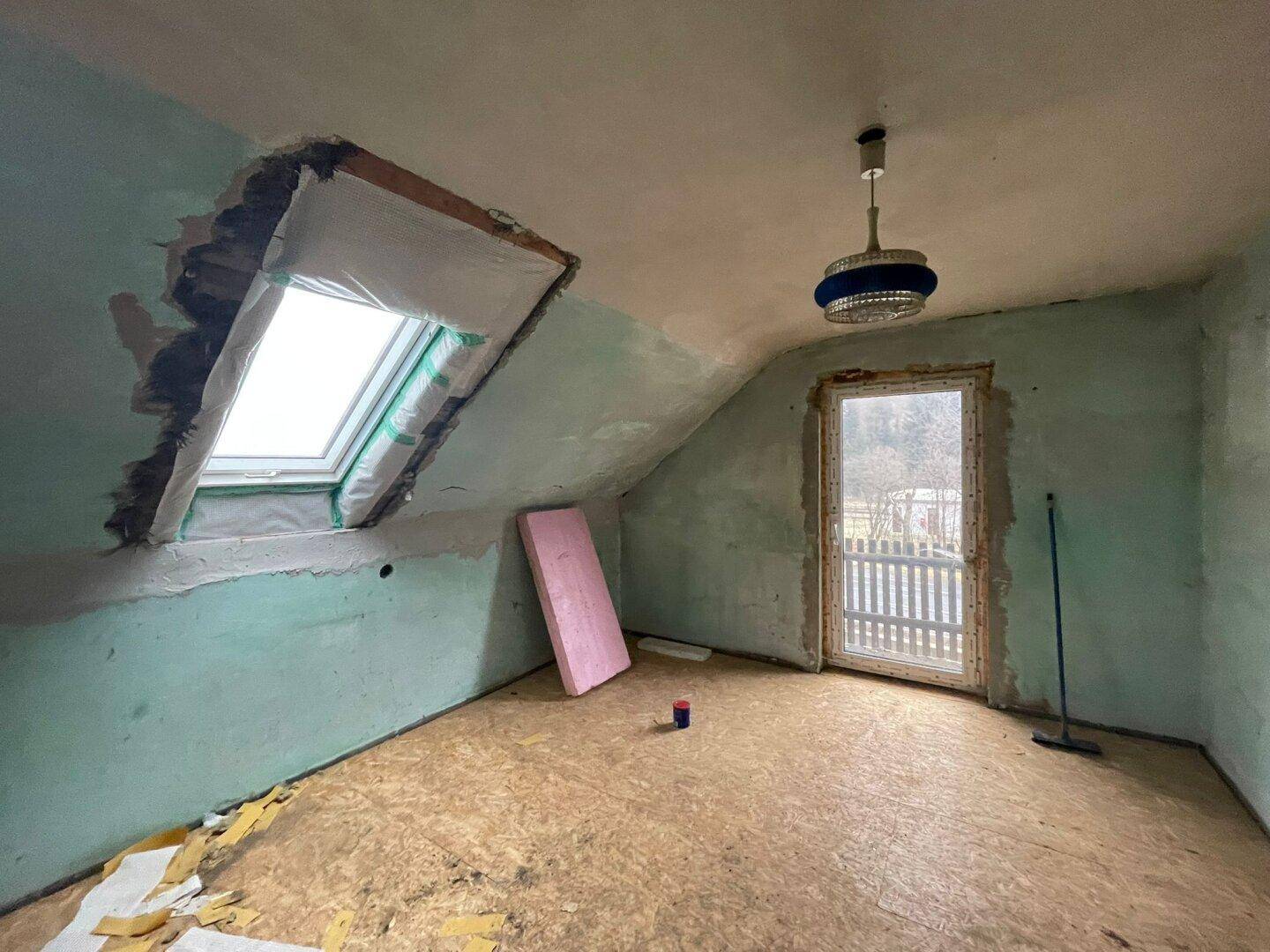 Dachgeschossraum in Renovierung mit Dachfenster und Zugang zu einem kleinen Balkon oder Garten.