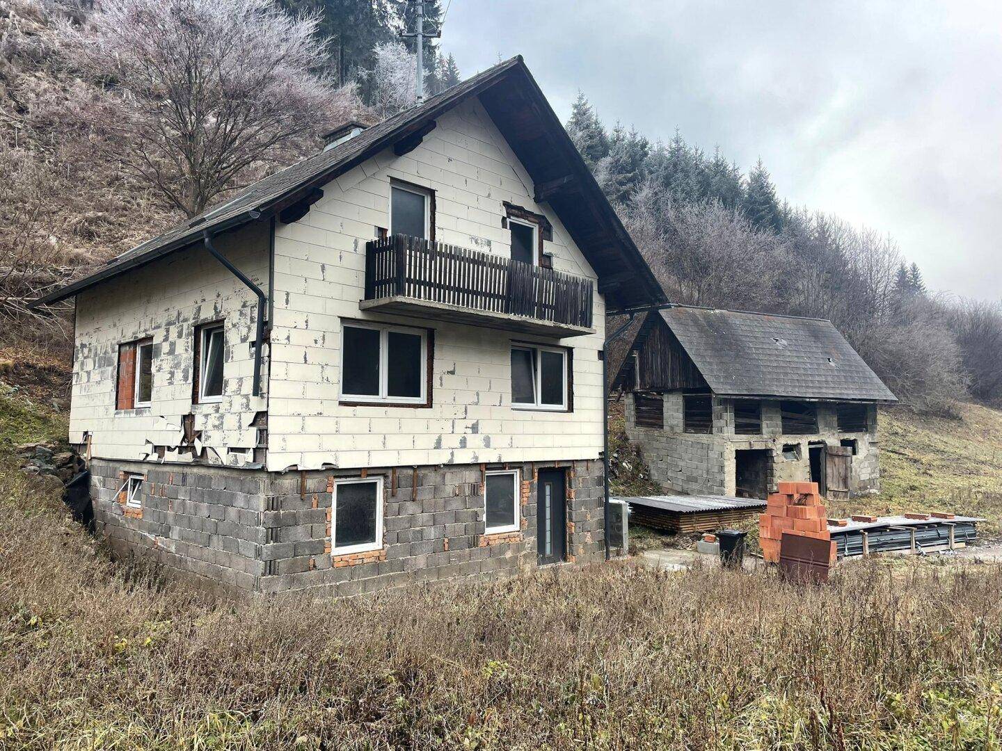 Wohnhaus und Nebengebäude in winterlicher Landschaft, umgeben von kahlen Bäumen und frostiger Natur.