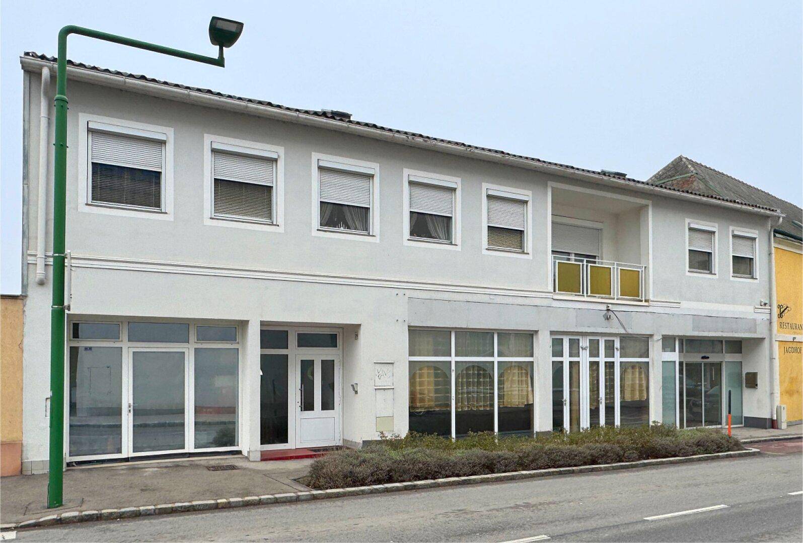 Ansicht der Gebäudefassade mit großen Schaufenstern im Erdgeschoss und Wohnungen im Obergeschoss.