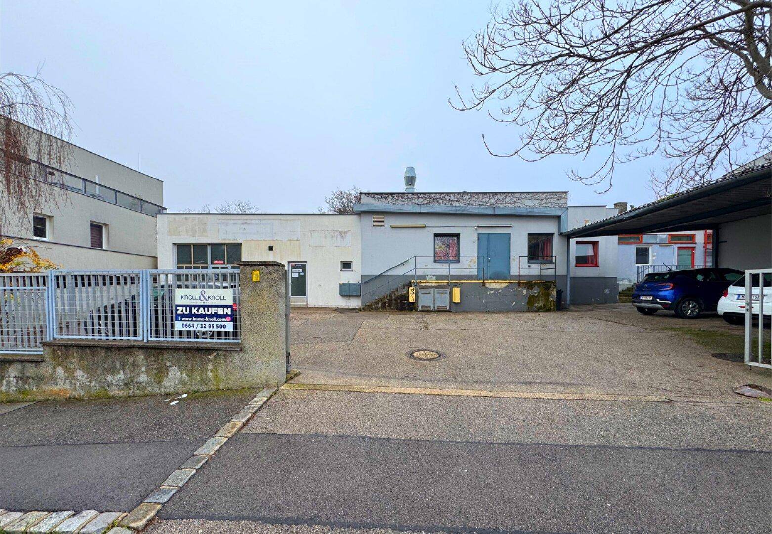 Rückansicht eines Gebäudes mit Parkplatz und einem "Zu Kaufen" Schild.
