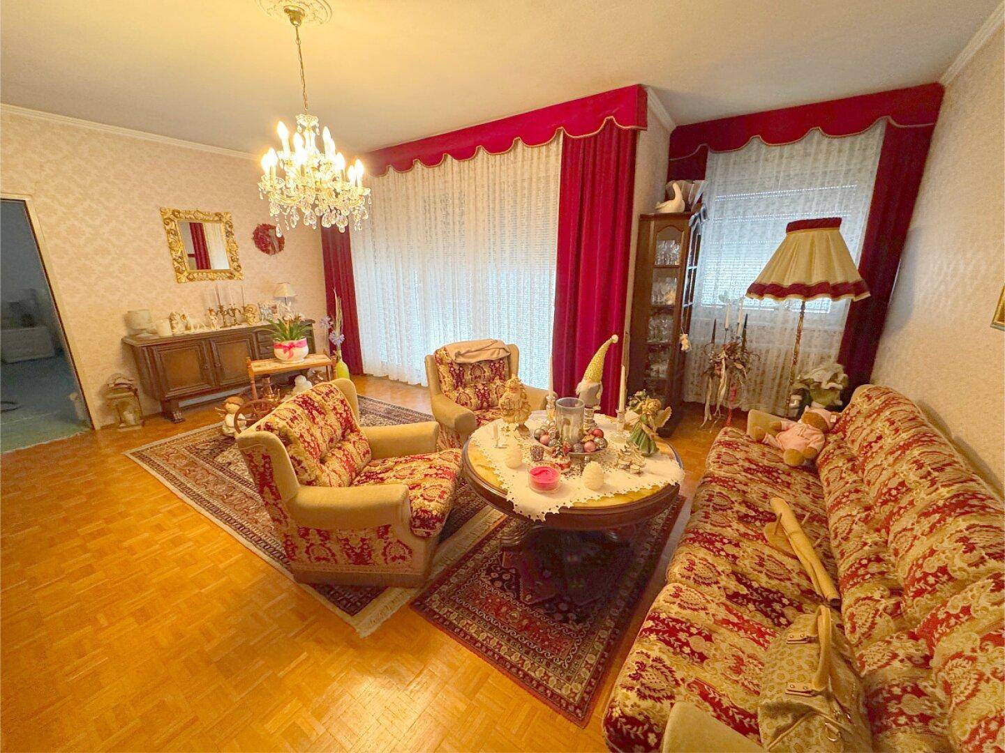 Geräumiges Wohnzimmer mit Parkettboden, bequemen Sesseln und einem Kronleuchter.