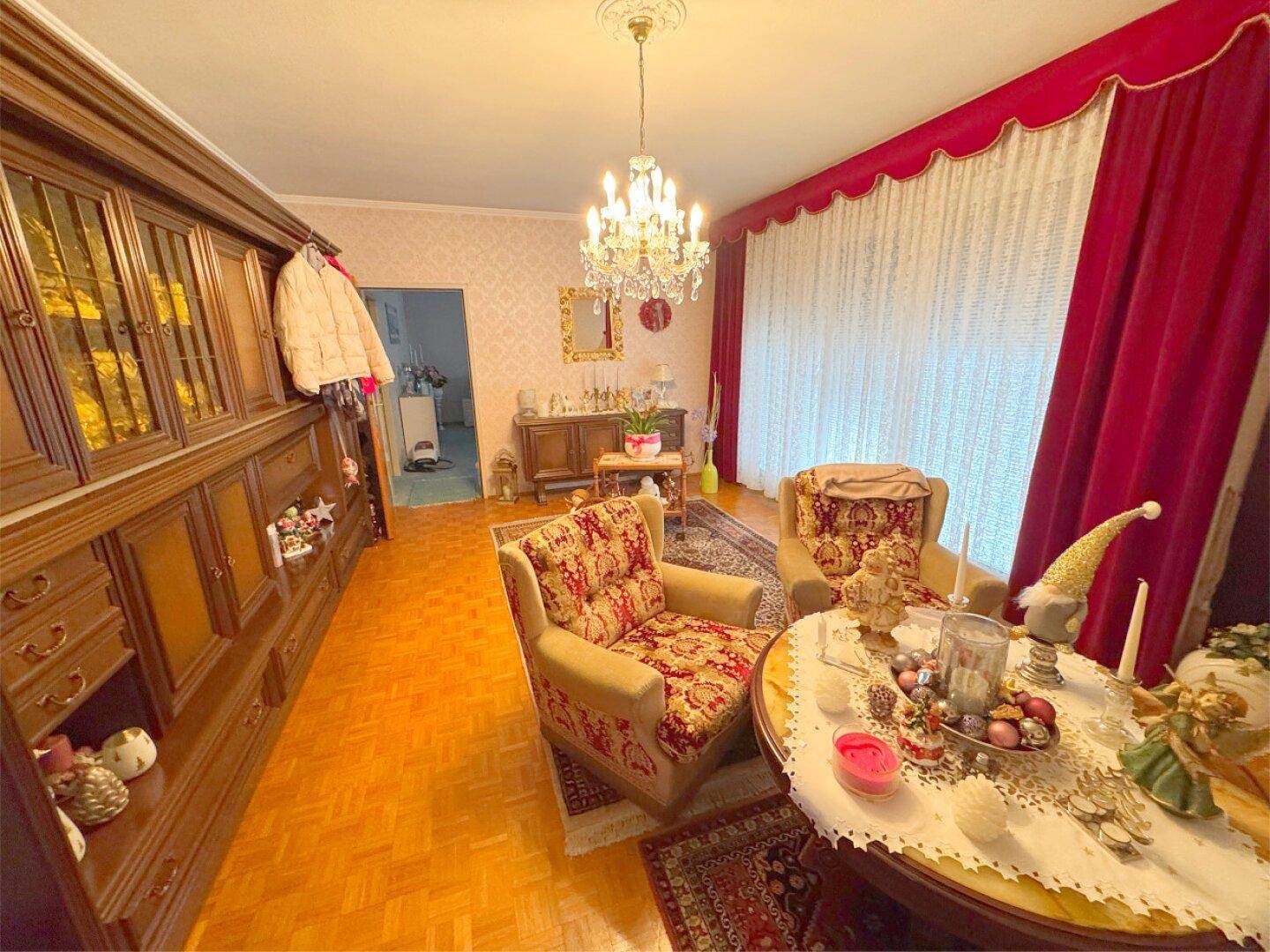 Elegantes Wohnzimmer mit Parkettboden, Kronleuchter und roten Vorhängen.