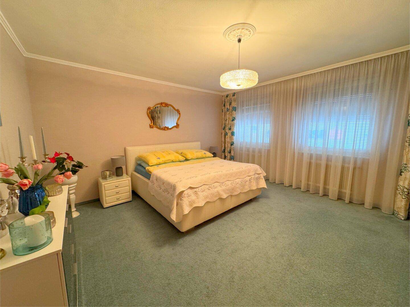 Schlafzimmer mit Teppichboden, Doppelbett und großen Fenstern mit Vorhängen.