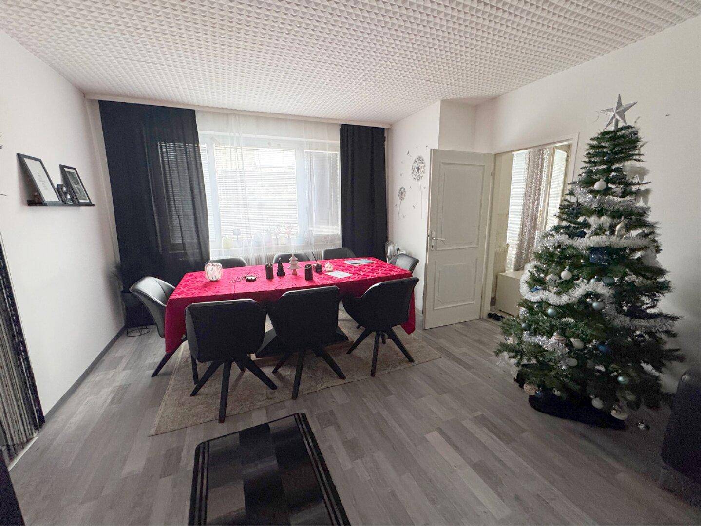 Esszimmer mit modernem Esstisch, Stühlen und einem Weihnachtsbaum.